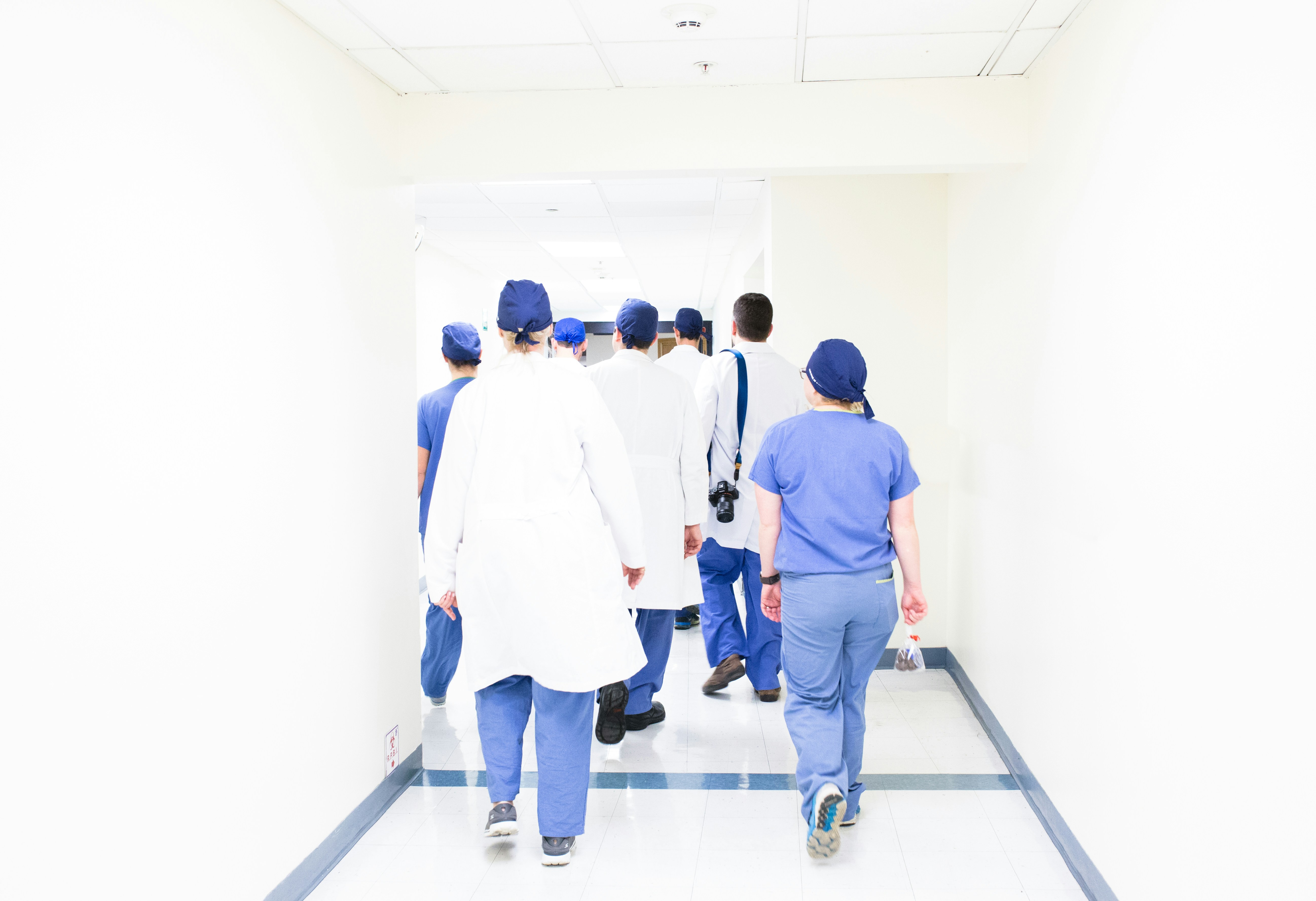 A group of healthcare professionals, including doctors and nurses walk through a brightly lit hospital corridor.
